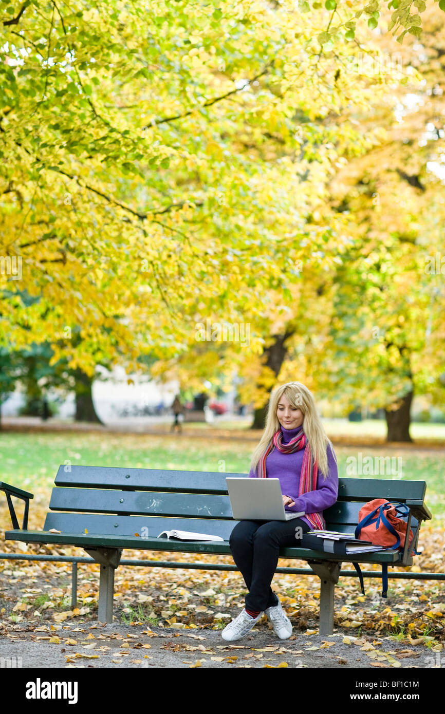 A woman sitting on a bench in a park using a laptop, Stockholm, Sweden. Stock Photo