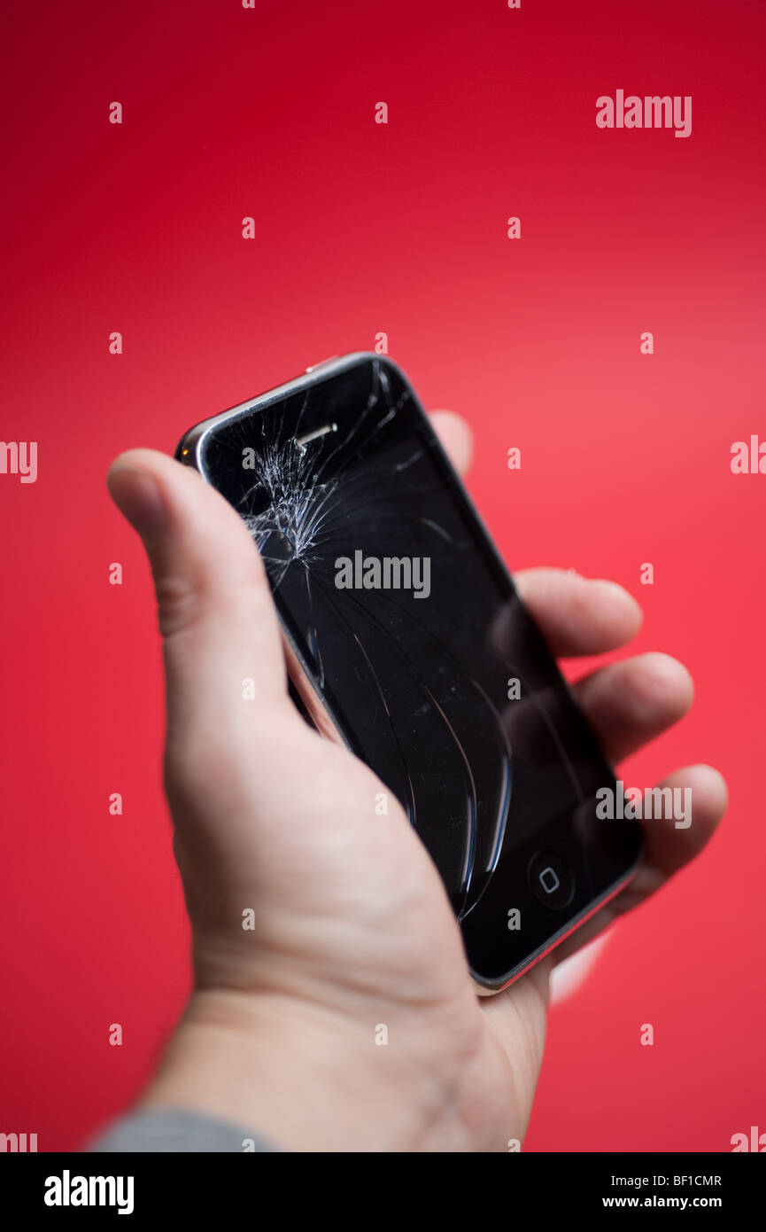 A damage Apple iPhone is held against a red background.  The screen has been heavily cracked. Stock Photo