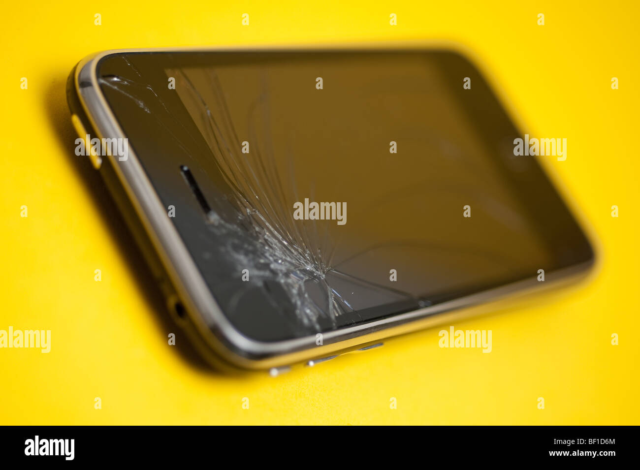 A damaged Apple iPhone device placed on a yellow backround.  The main control screen has been cracked at the top. Stock Photo