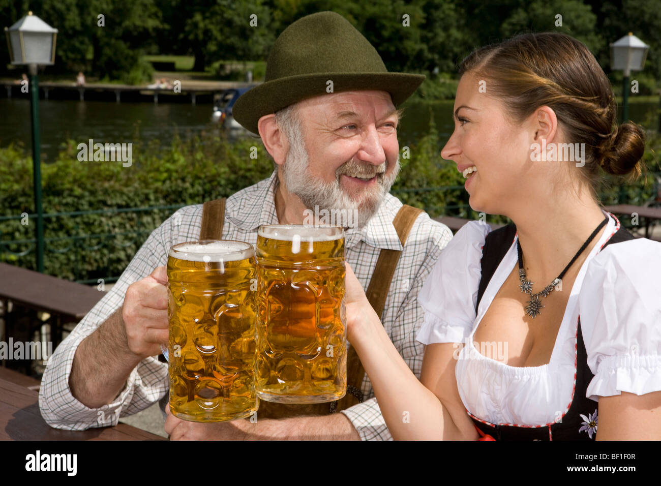 A traditionally clothed German man and woman in a beer garden toasting glasses Stock Photo