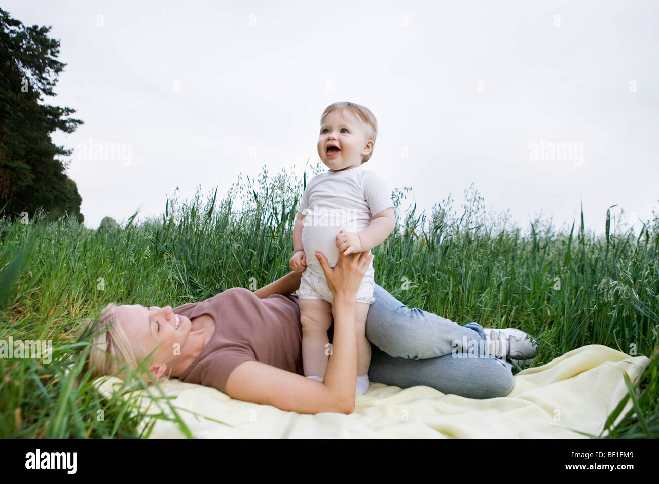 A mother and baby daughter playing on a rug in a field Stock Photo