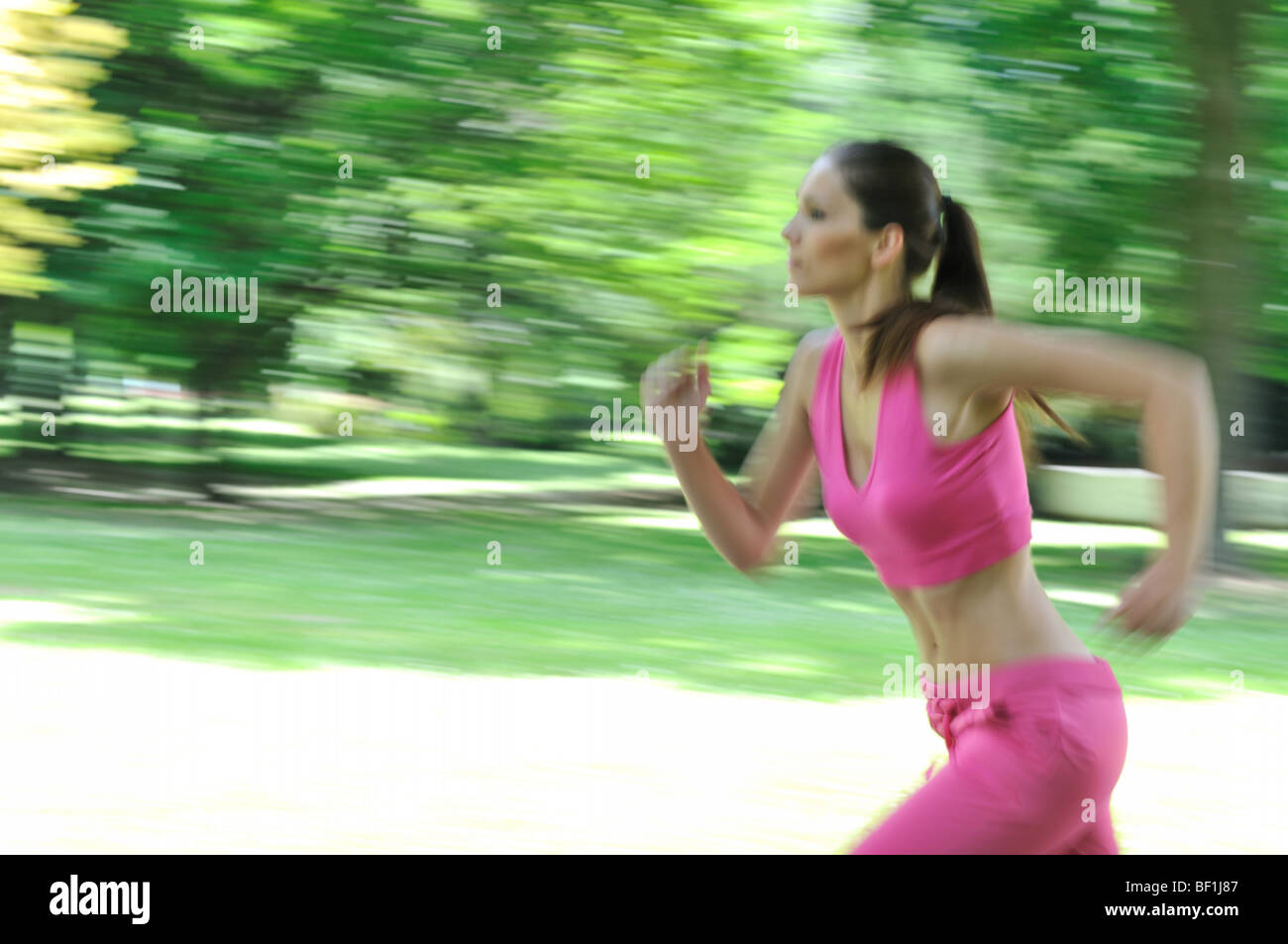 Young person (woman) running outside in park on sunny day - motion blurr Stock Photo