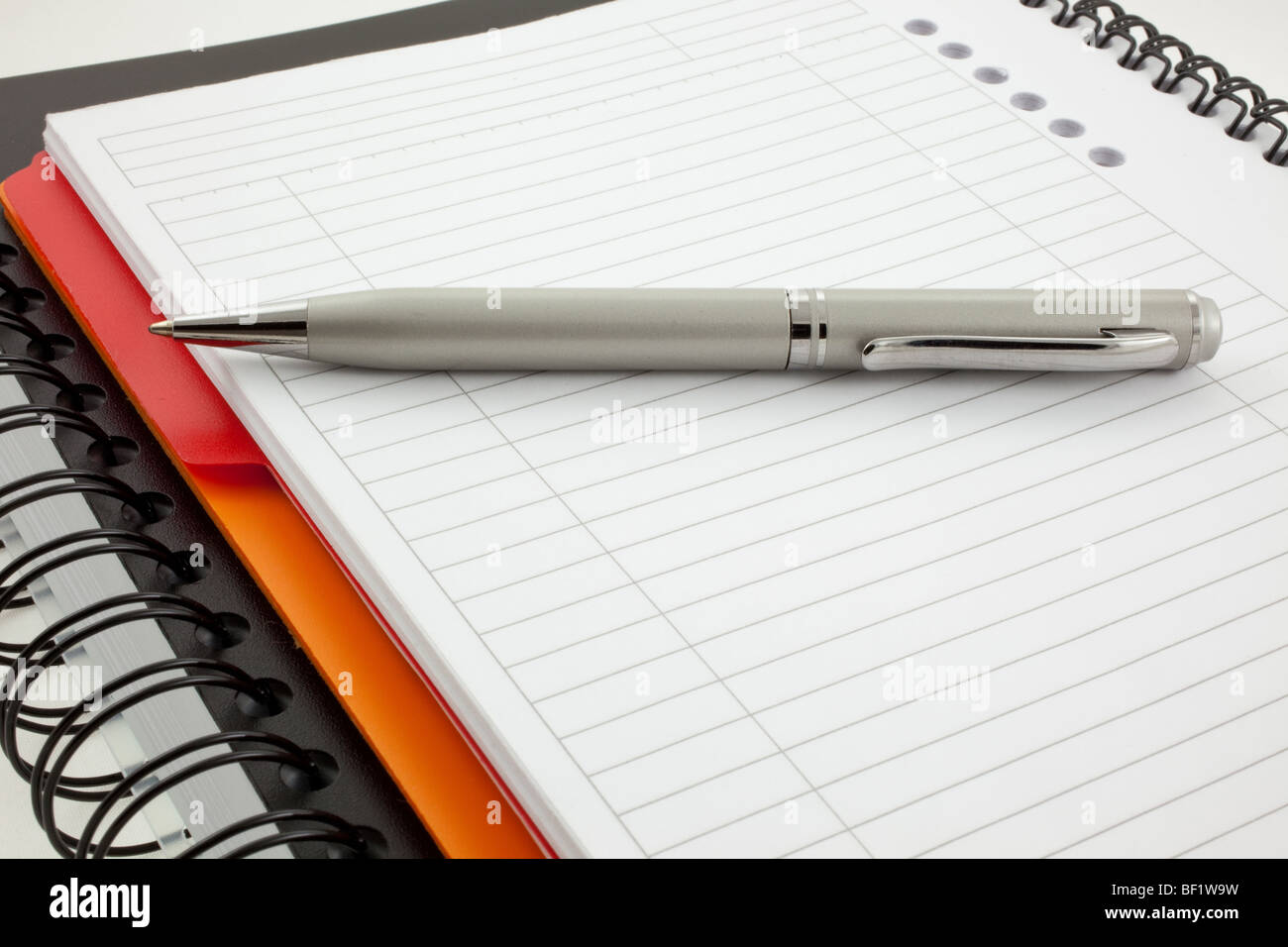 silver pen and two paper notebooks: orange and black Stock Photo