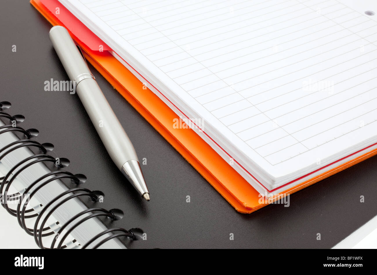 silver pen and two paper notebooks: orange and black Stock Photo