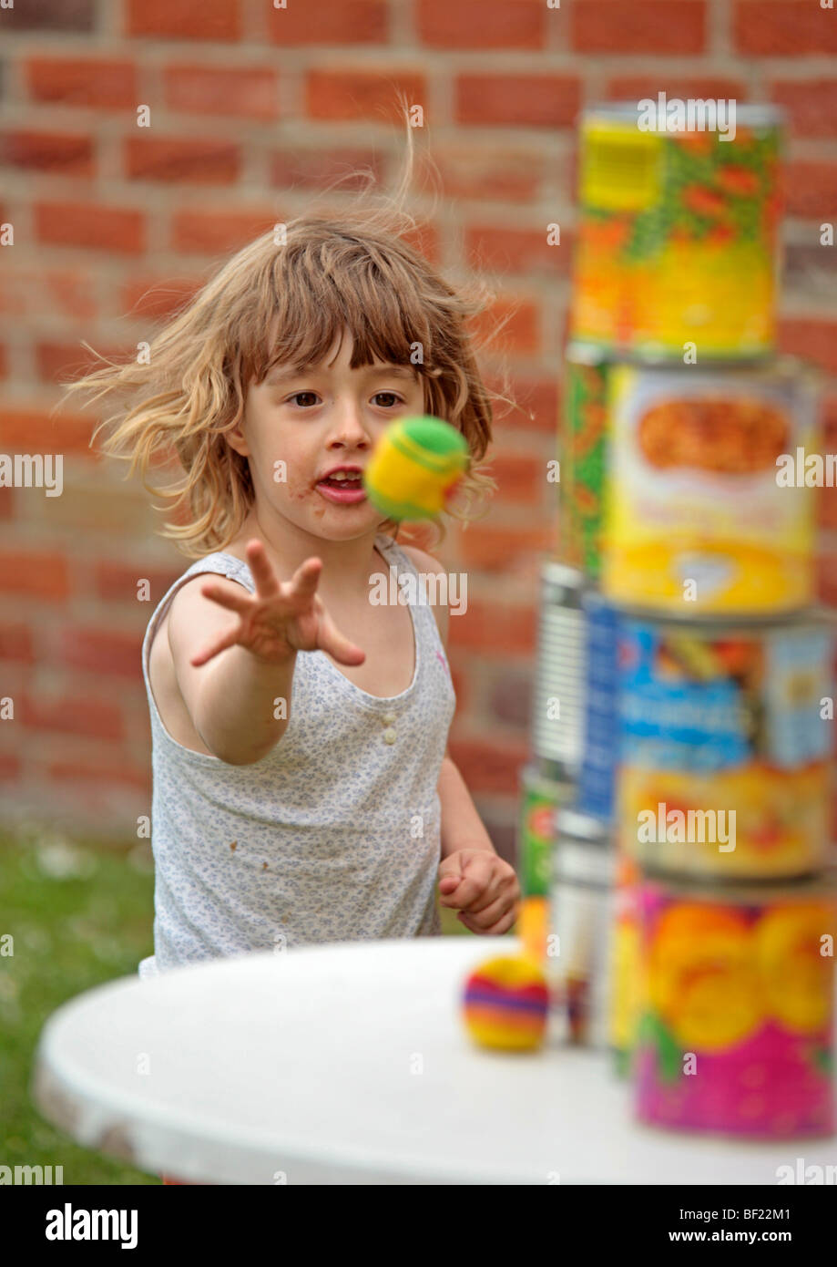 a young girl throwing a ball at a pyramid of cans at a children's birthday party Stock Photo