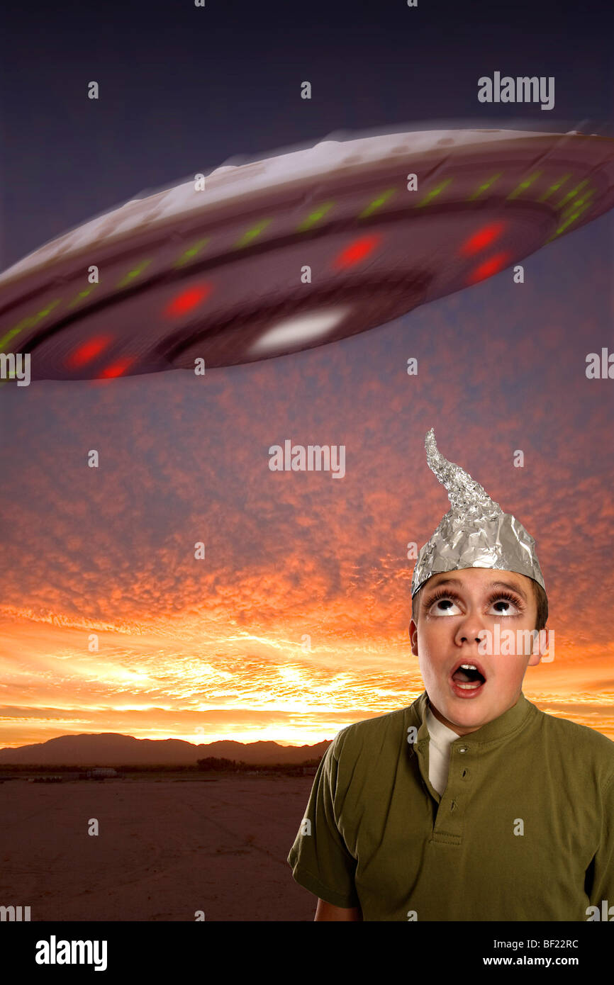 A bug-eyed boy, wearing a tin-foil hat observes a UFO in the sky. Stock Photo