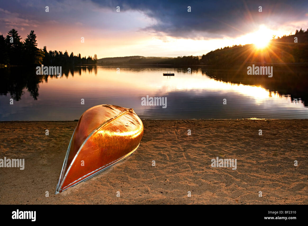 Sun setting over tranquil lake with canoe on beach Stock Photo