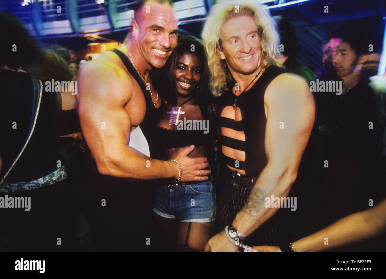 London Ministry of Sound, club, black girl smiling and wearing cross dancing and posing with two muscular white men Stock Photo