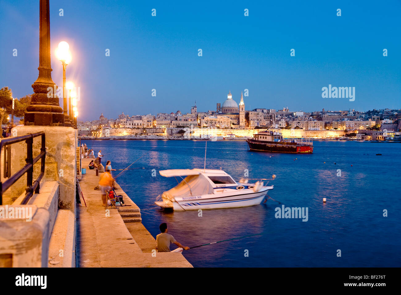 Anglers sitting on the promenade in the evening, view at the town of Valletta, Sliema, Malta, Europe Stock Photo