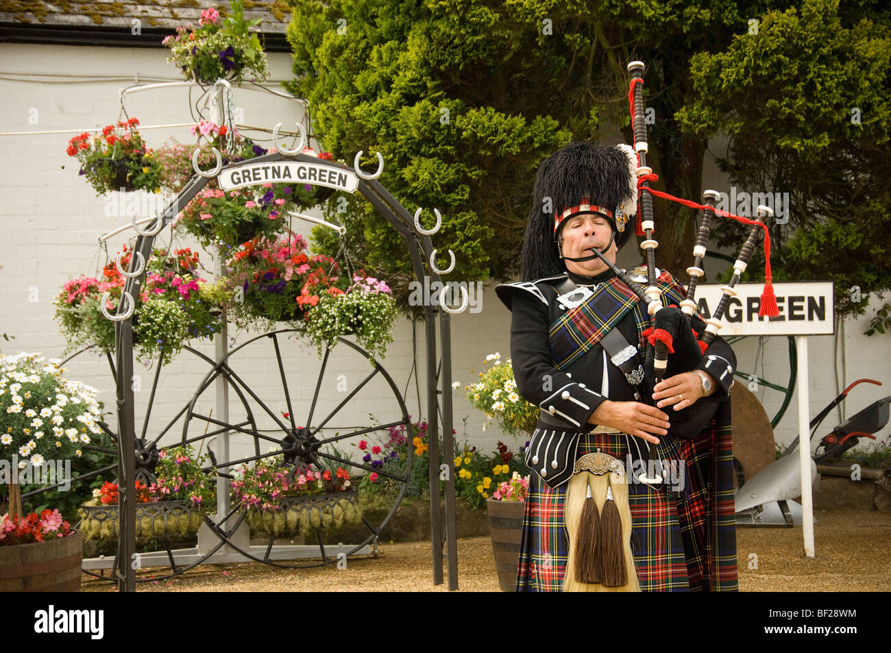 Caucasian Scottish male piper playing bagpipes outside the Gretna Green Old Blacksmith's shop, Scotland. UK Stock Photo