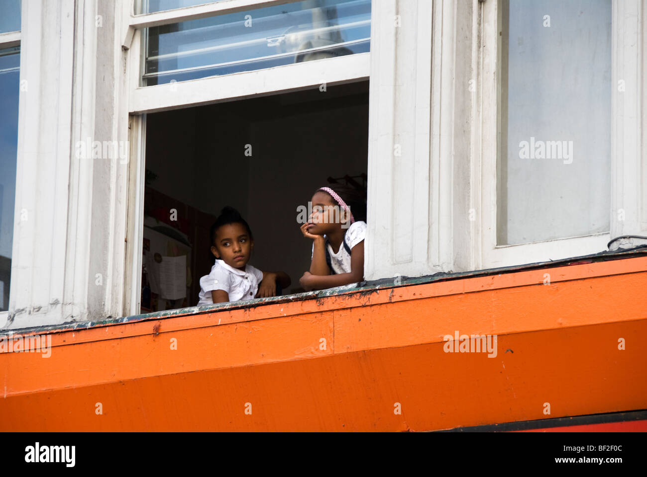 Two young children sitting in window watching Notting Hill carnival below Stock Photo