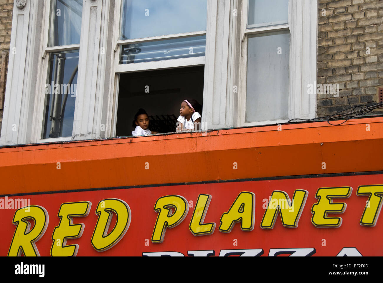 Two young children sitting in window watching Notting Hill carnival below Stock Photo