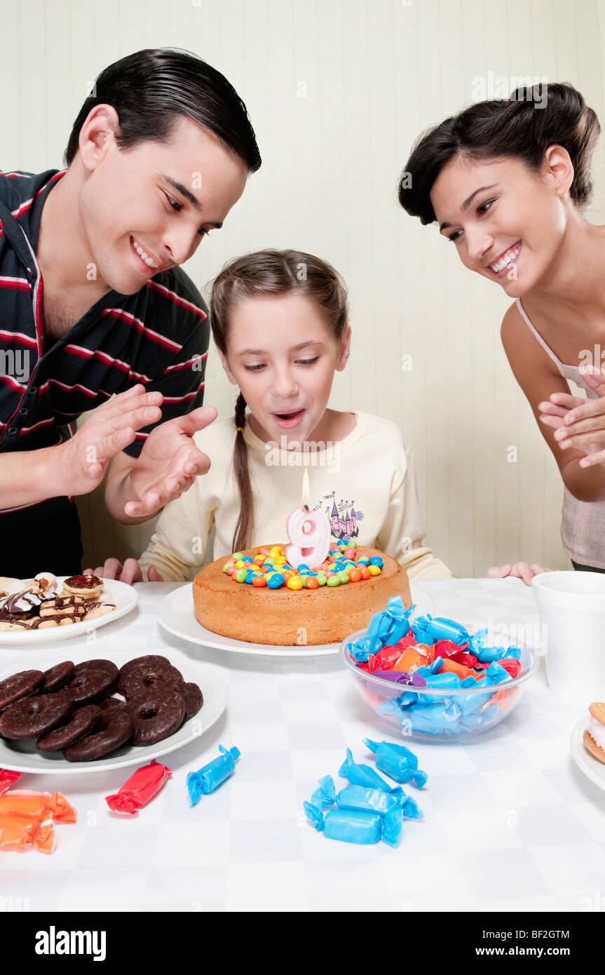 Girl blowing out birthday candle with their parents Stock Photo
