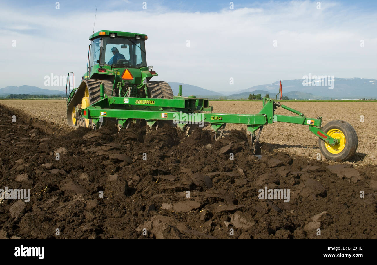 A John Deere tracked tractor pulling a moldboard plow prepares a seedbed for planting potatoes / Burlington, Washington, USA. Stock Photo