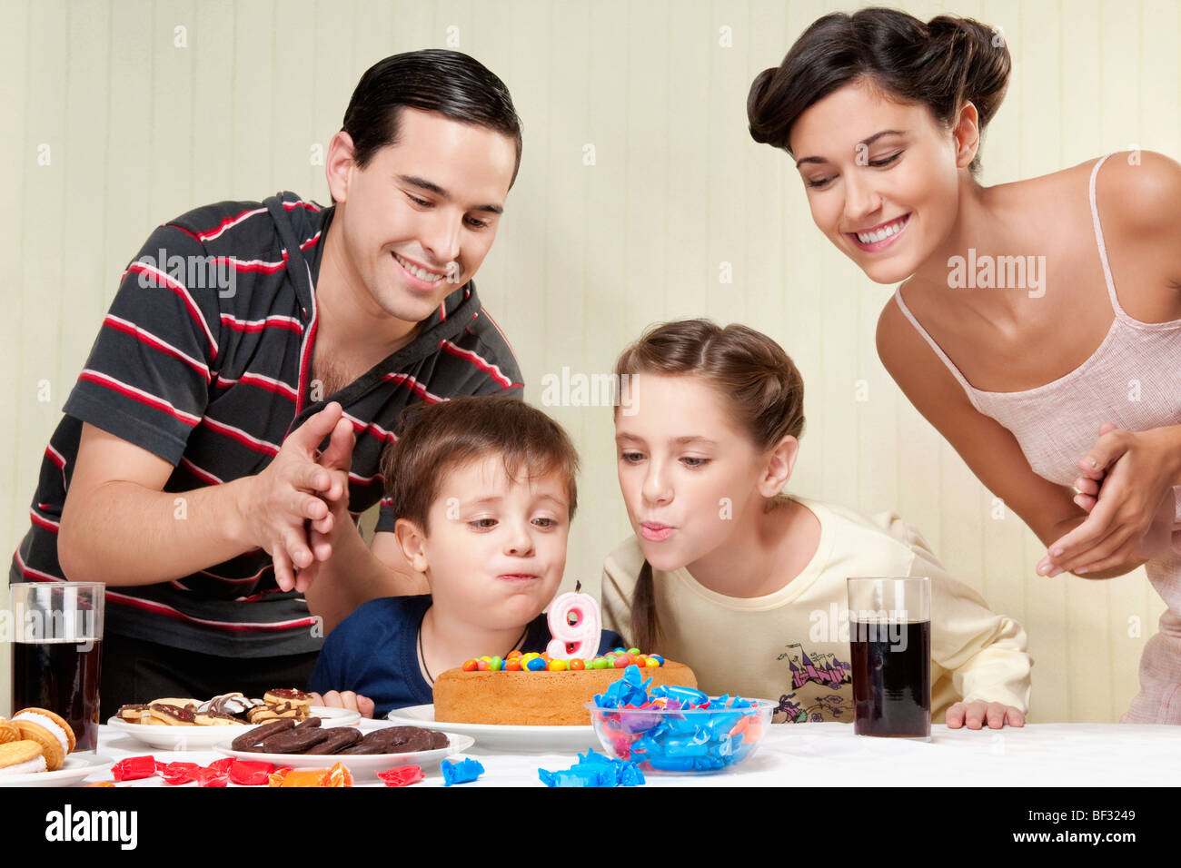 Boy and a girl blowing out birthday candles with their parents Stock Photo