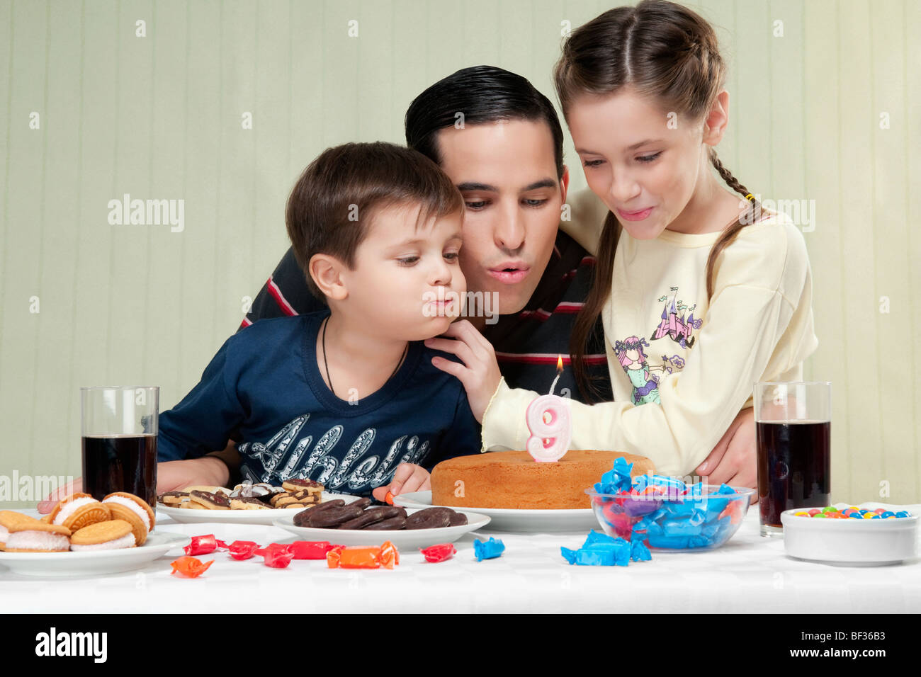 Boy and a girl blowing out birthday candles with their father Stock Photo