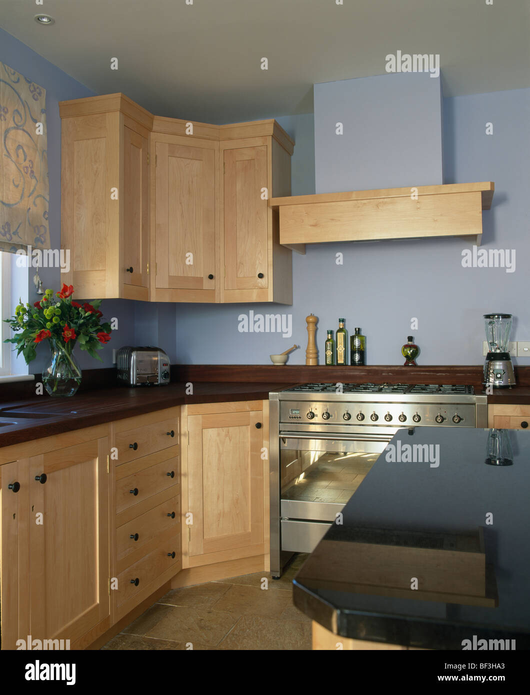Modern pastel blue kitchen with pale wood fitted units and stainless
