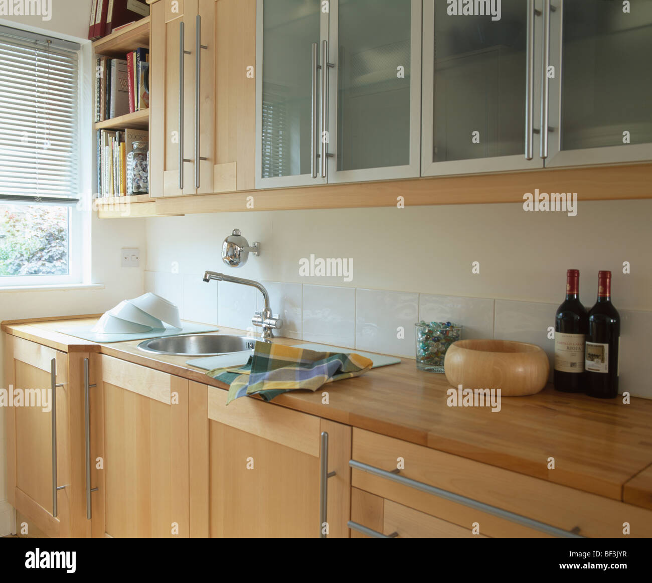 Fitted cupboards with glazed doors above sink set into pale wood units