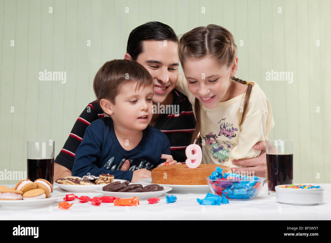 Boy and a girl blowing out birthday candles with their father Stock Photo