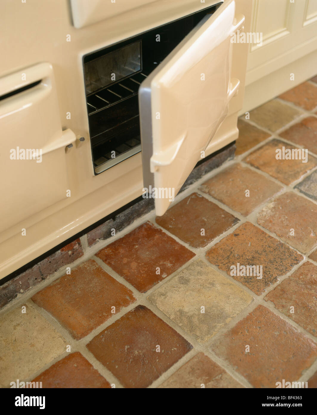 Close-up of cream Aga oven with open door above terracotta floor tiles Stock Photo