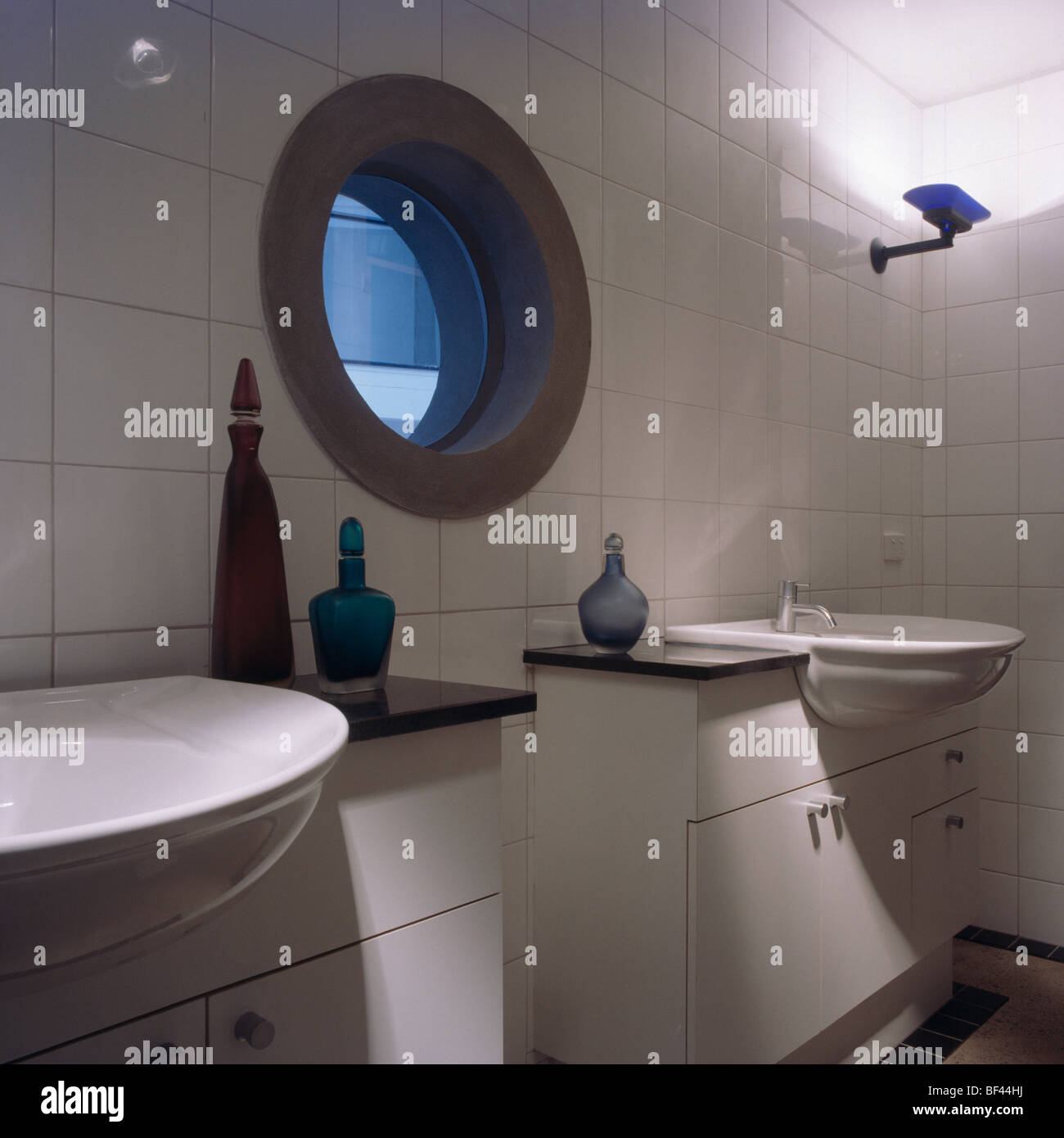 Circular window in modern white tiled bathroom with double basins and