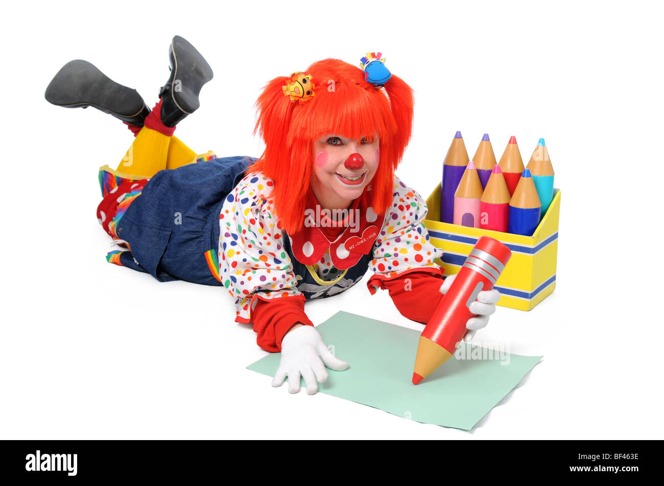 Clown laying down on the floor and writing with large color pencils Stock Photo
