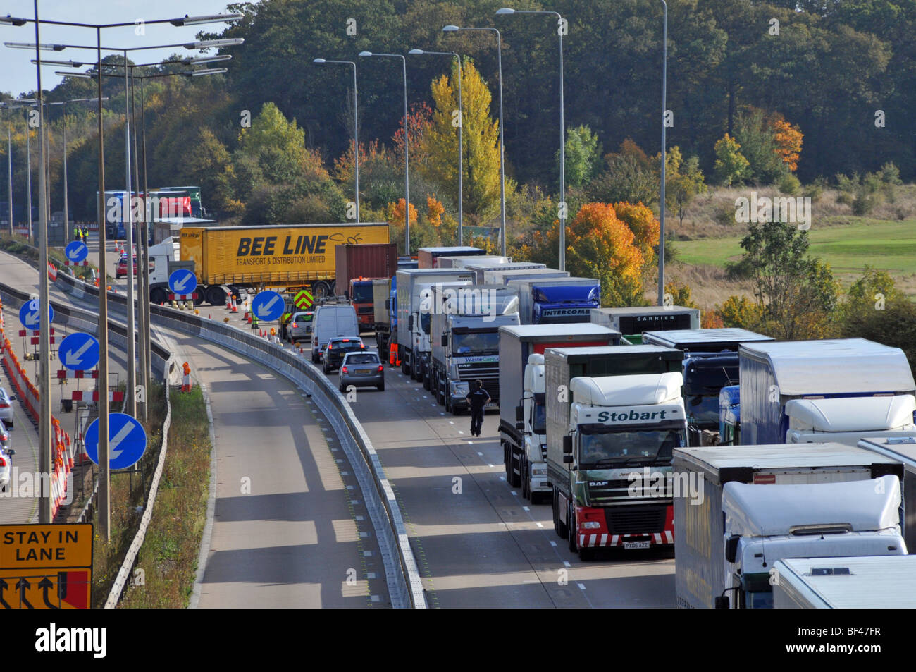 Police distant turning around gridlocked lorries & other traffic on M25 motorway roadworks section after closing due to accident Stock Photo