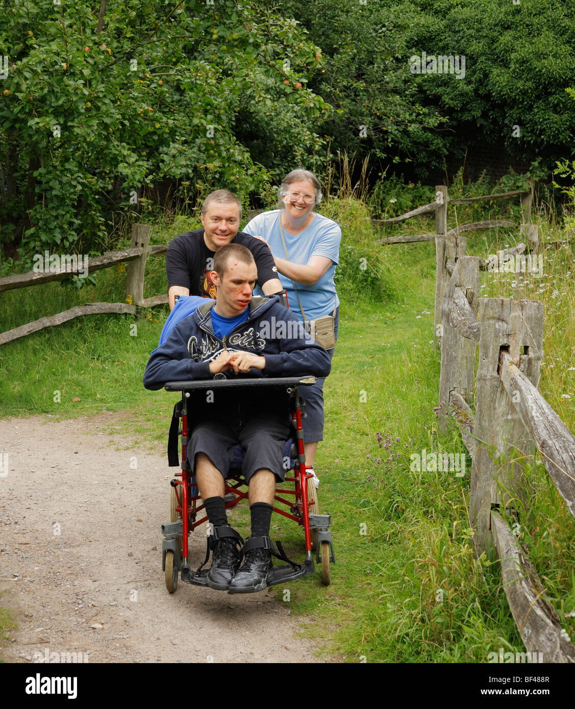 Disabled boy being pushed along by loving parents. Stock Photo