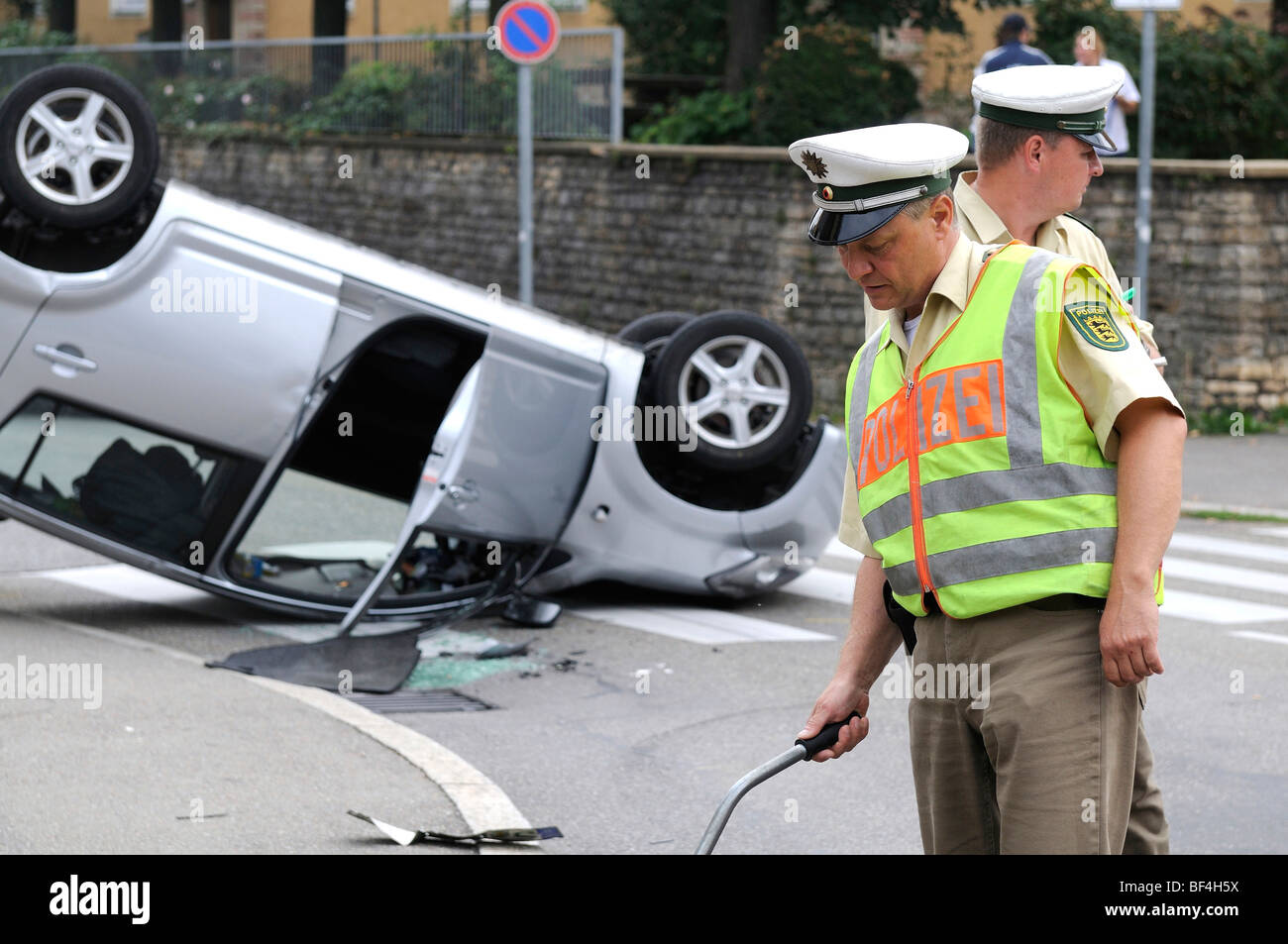 Daihatsu car having rolled over in a traffic accident, lying on its roof, police officer writing up the accident, surveying, St Stock Photo
