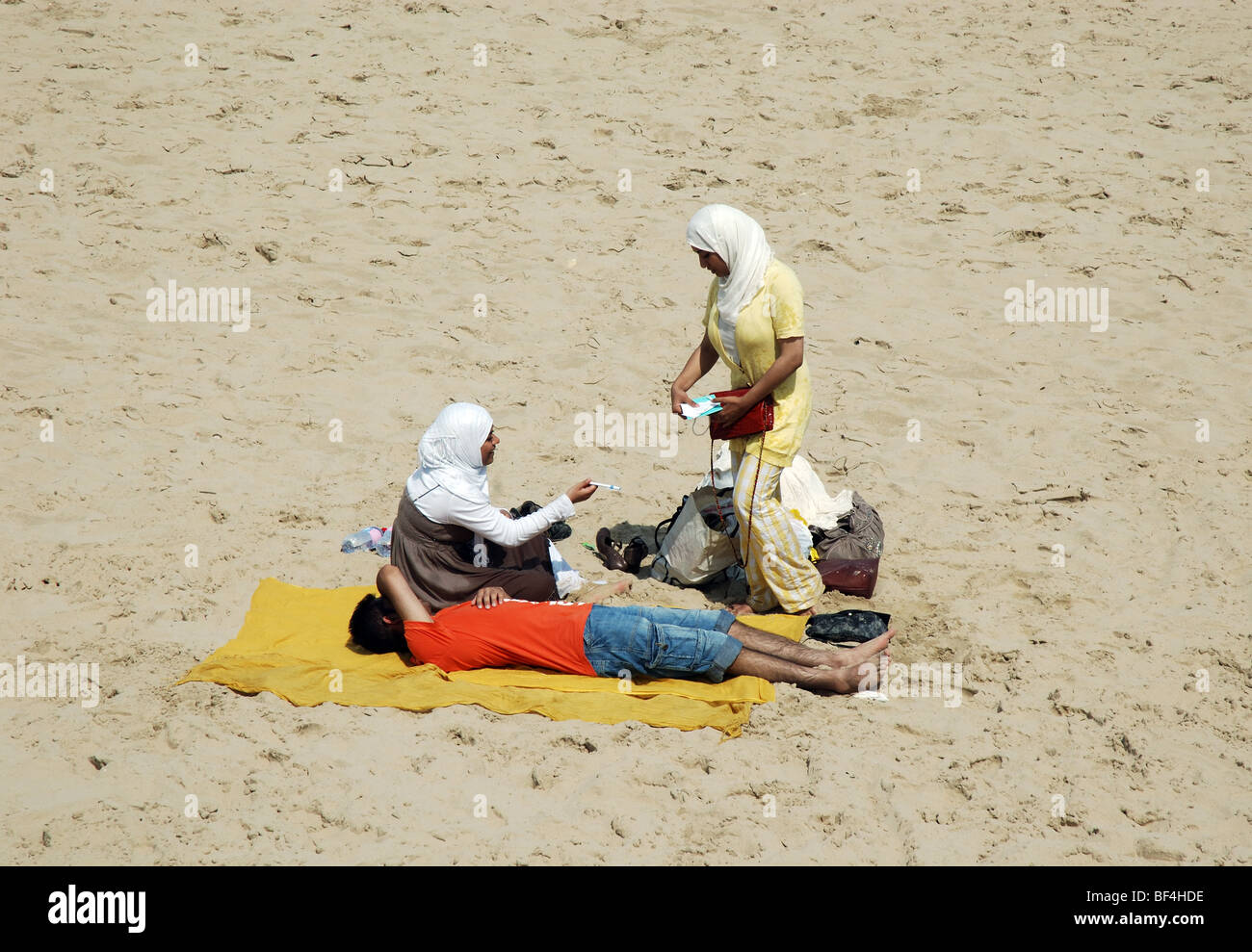three muslim people relaxing on Bournemouth beach, Hampshire, England, UK Stock Photo