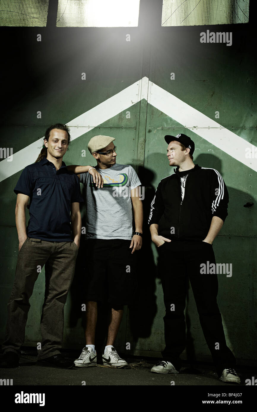 Portrait of three young men standing in front of an old steel door ...