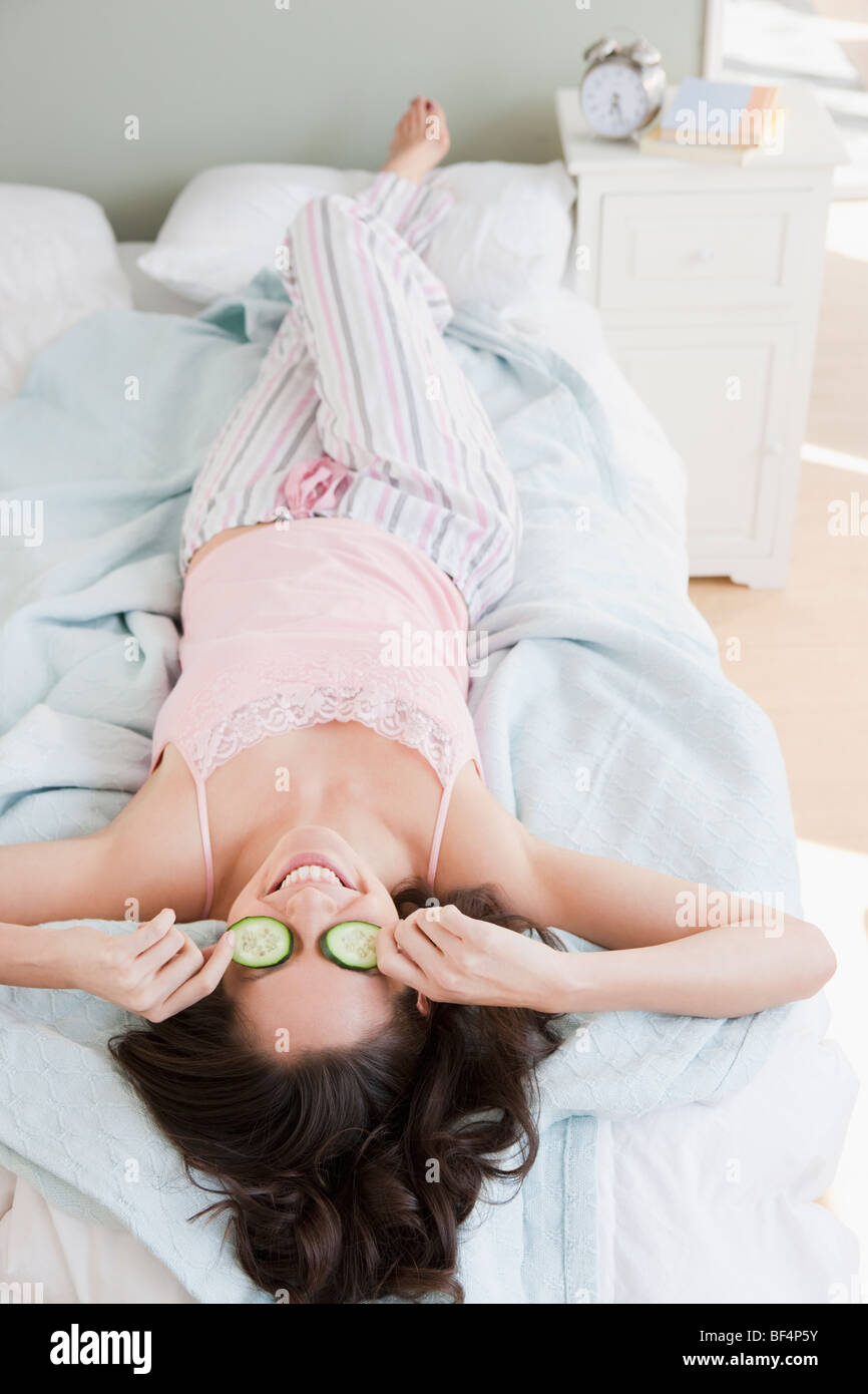 Mixed race woman placing cucumbers over eyes in bed Stock Photo Alamy