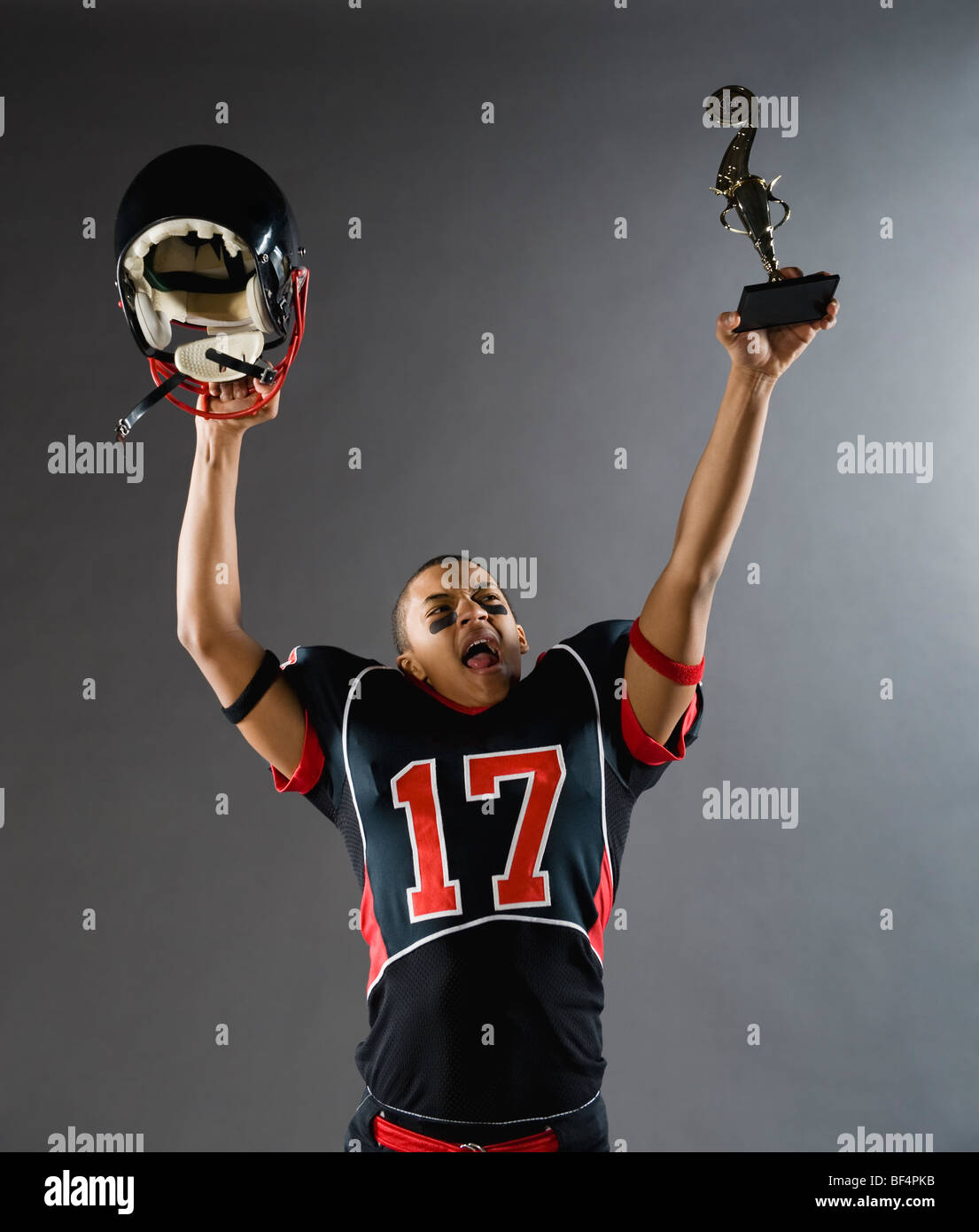 Mixed race football player holding helmet and trophy overhead Stock Photo