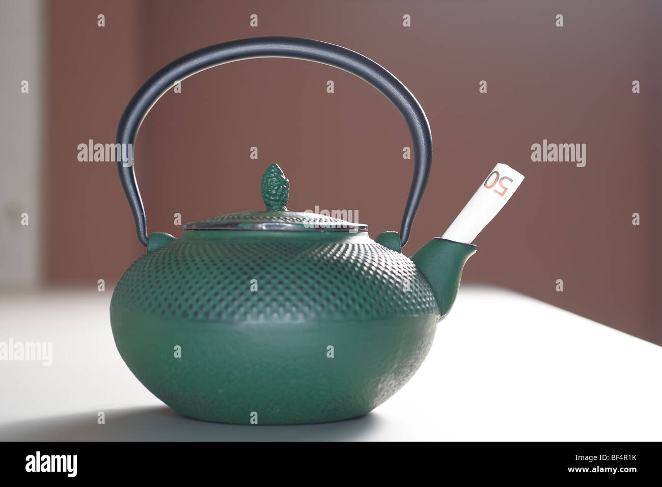 Cast iron teapot with a banknote in the pouring spout Stock Photo