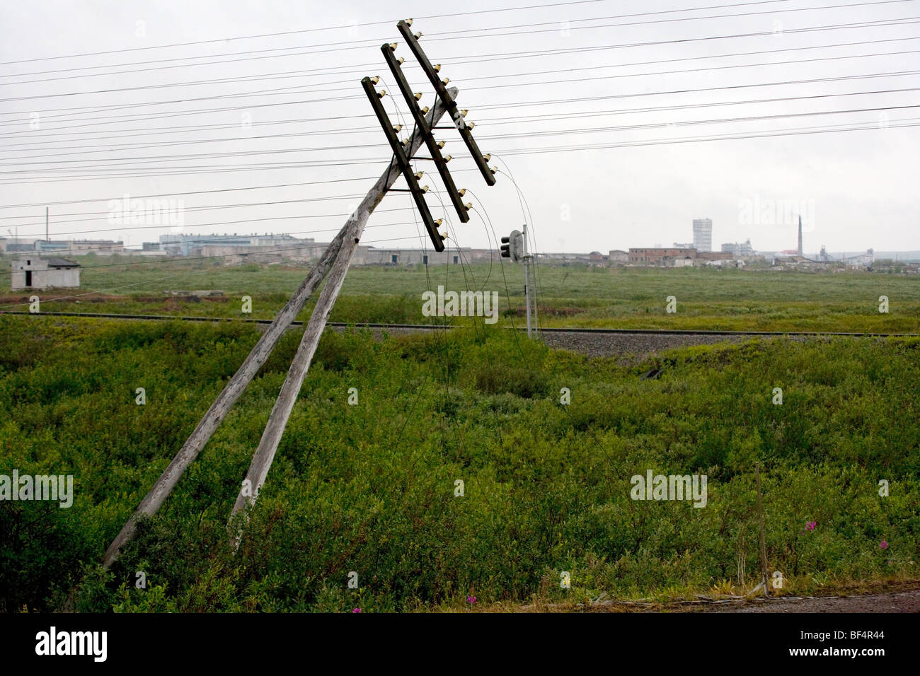 Fallen telegraph pole with industrial buildings and smoke stacks on horizon, Urals, Arctic Russia Stock Photo