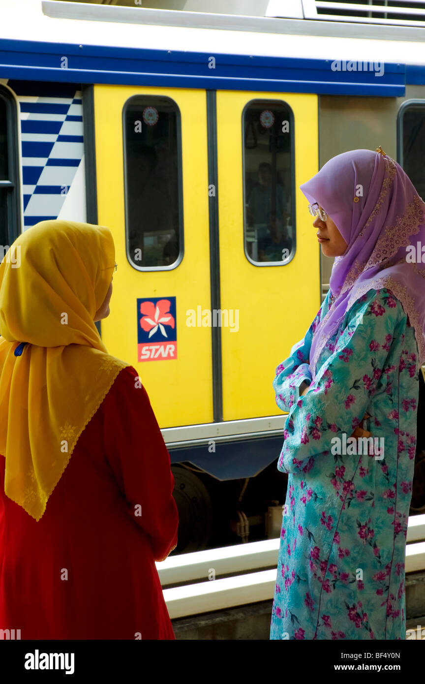Colourful female Islamic commuters in hijab chat as they wait at a station. Kuala Lumpur, Malaysia Stock Photo