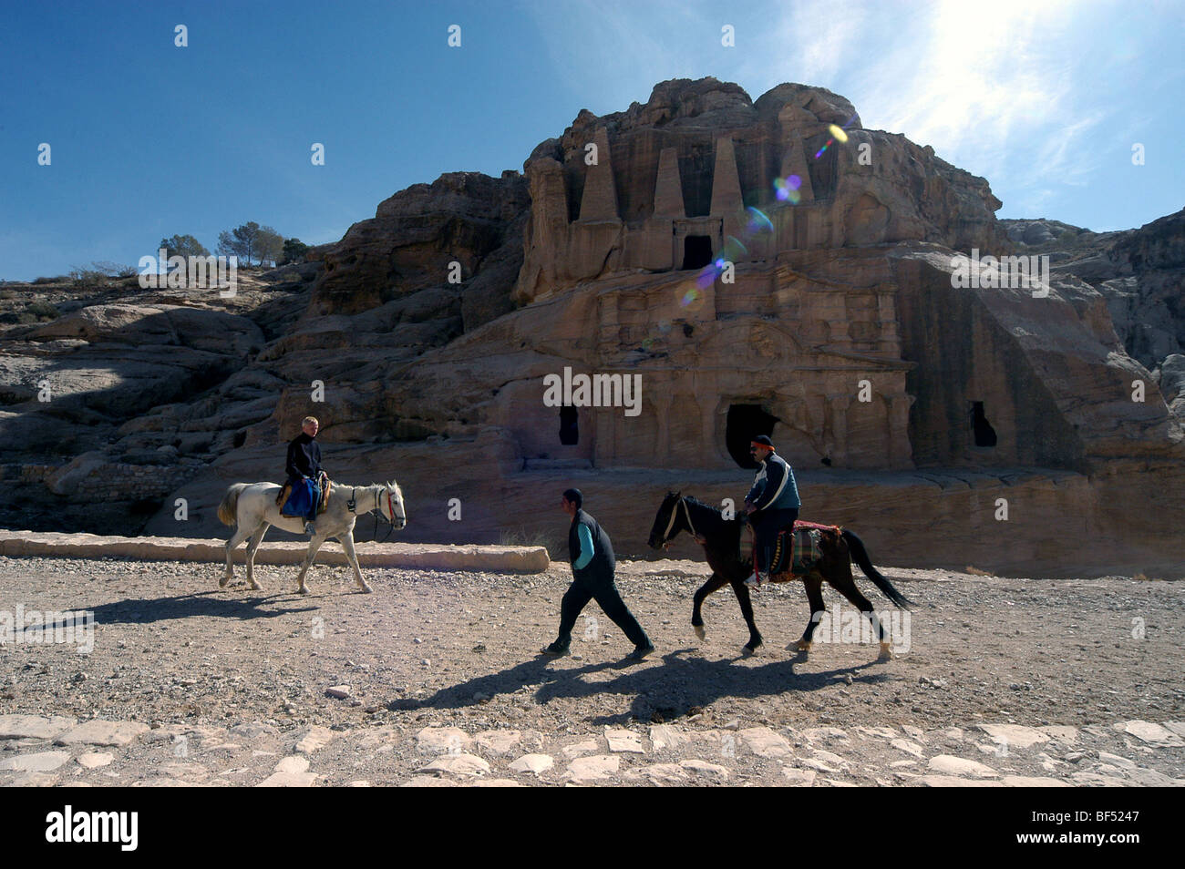 Horses and riders pass the Obelisk tomb at the entrance to Petra, Jordan Stock Photo
