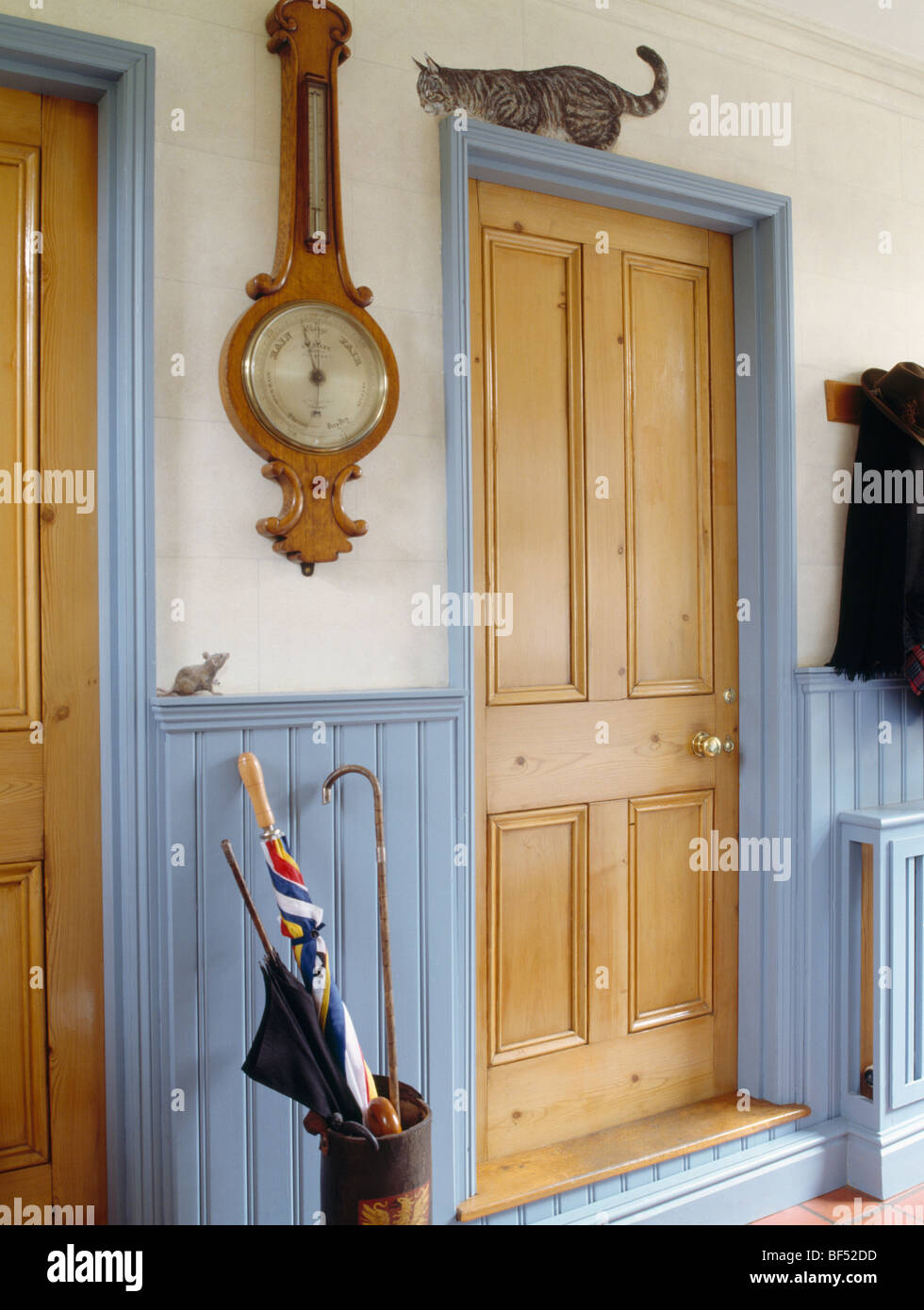Barometer on wall above pastel blue dado panelling in small hall with trompe-l'oiel cat above pine door Stock Photo