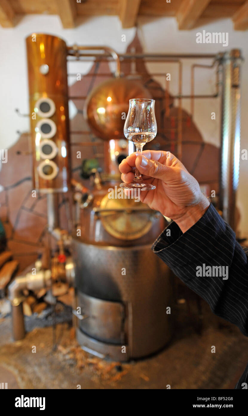 Hand holding jigger in front of a distillery, house distillery, Berg
