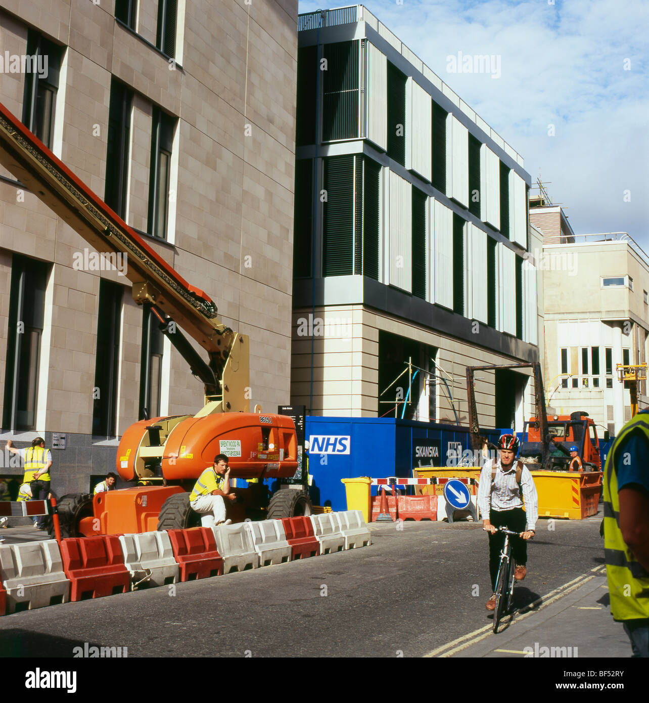Cyclist riding past NHS St. Barts new hospital construction site and workers in London England UK  KATHY DEWITT Stock Photo