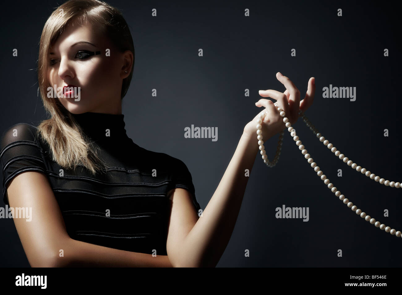 Young blonde woman wearing a black dress holding a pearl necklace in her hand, Fashion Stock Photo