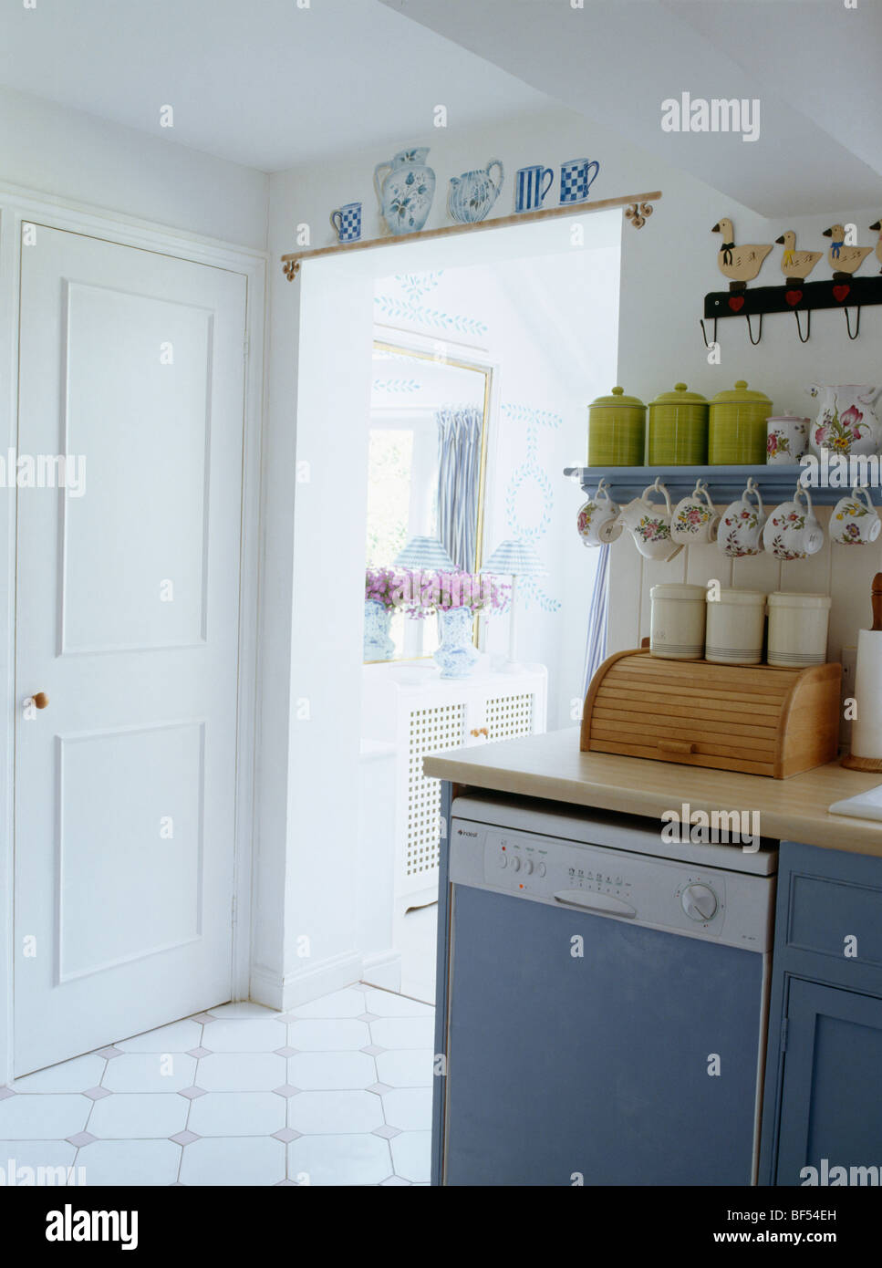 Small storage shelves above worktop on fitted unit with dishwasher in white cottage kitchen Stock Photo