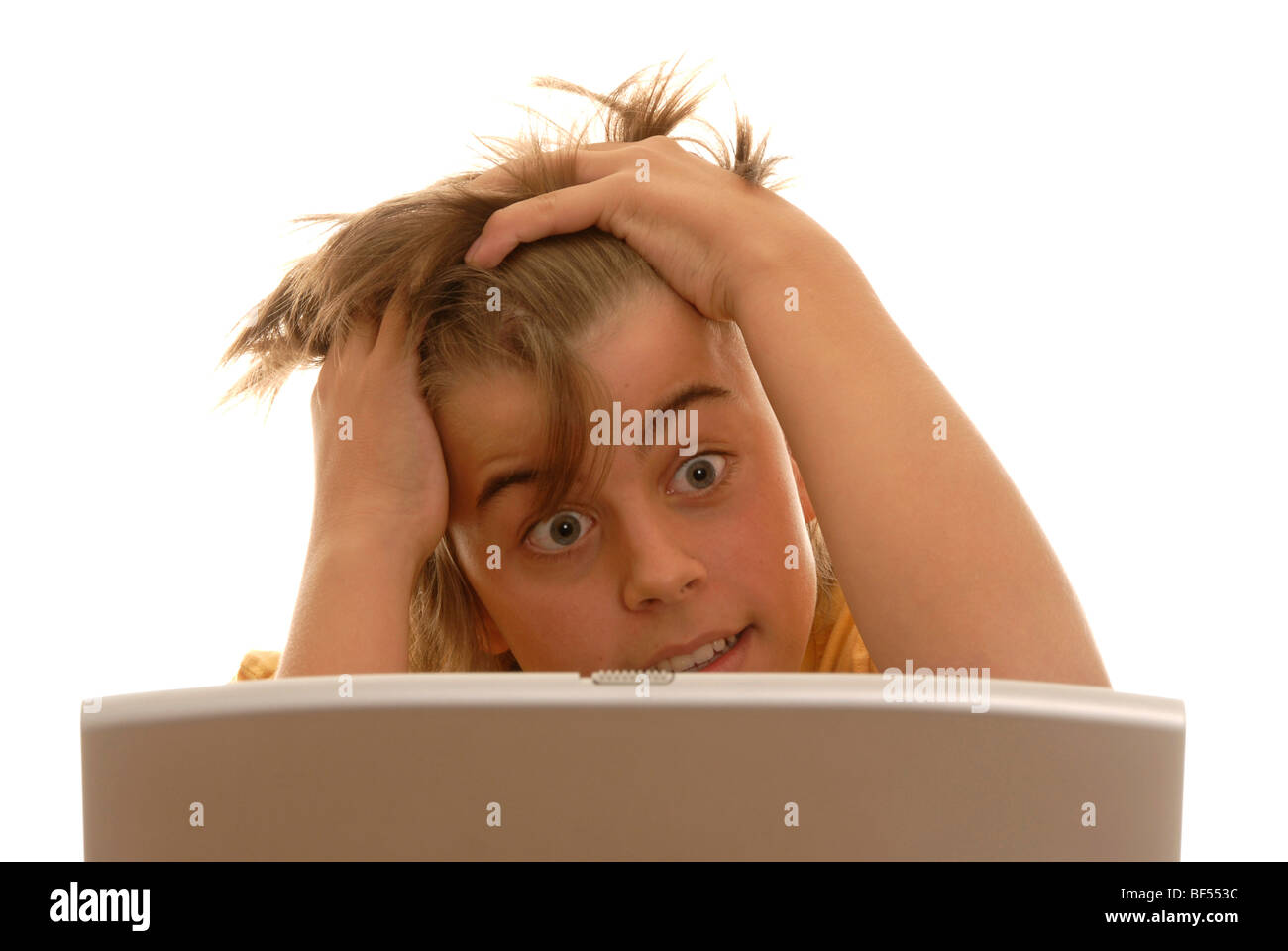 Boy, 16, behind a laptop desperately tearing at his hair Stock Photo