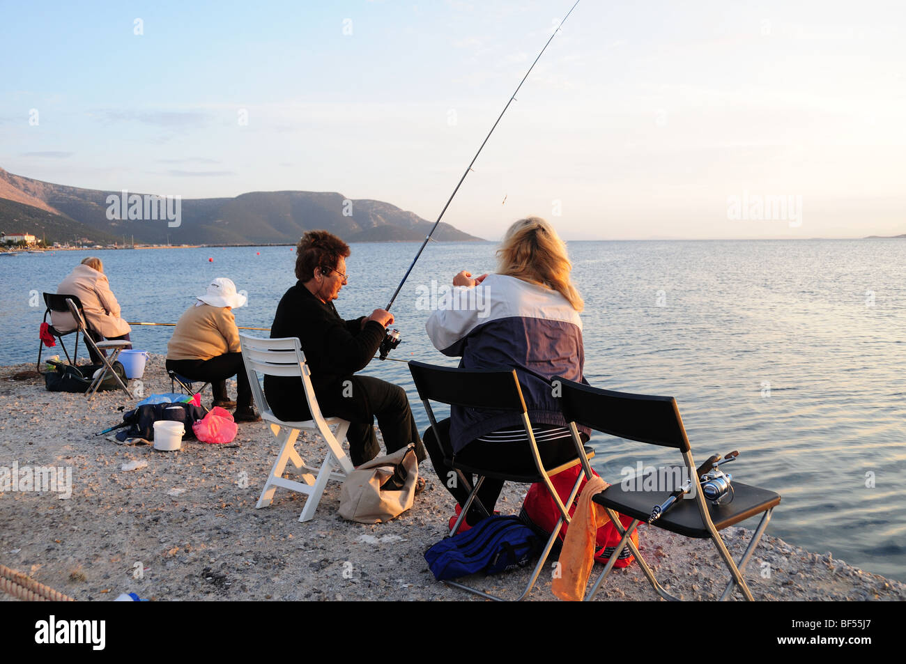 Four Greek women fishing in the sunset Marmari Harbour Evia Greece Stock Photo