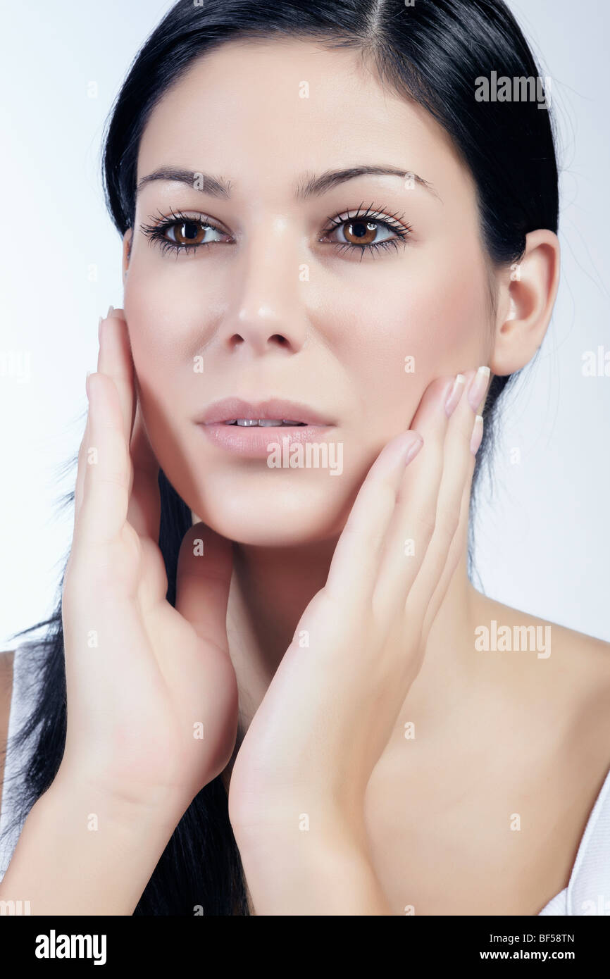 Young dark-haired woman stroking with both hands over her cheeks, beauty Stock Photo