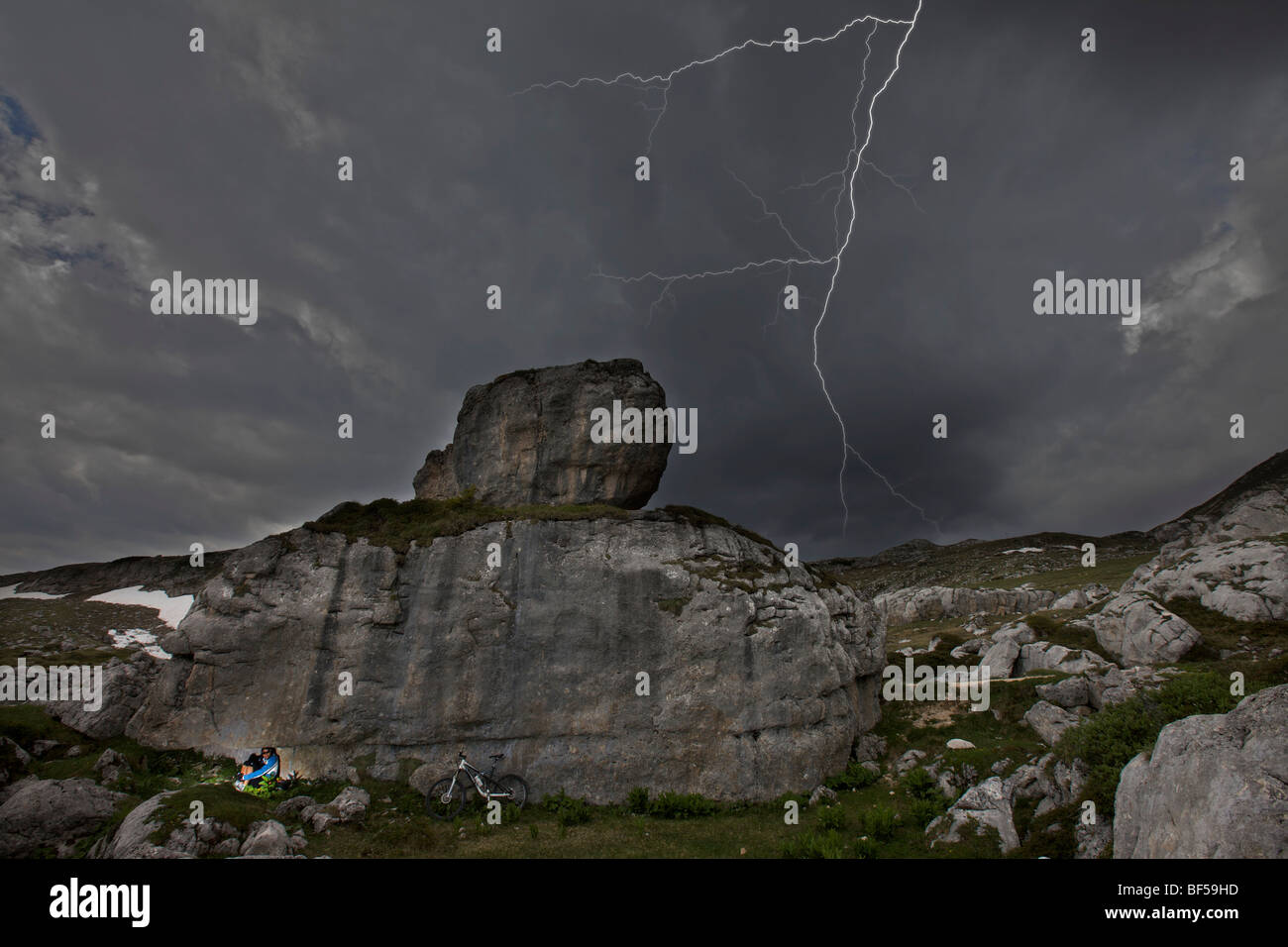 Mountain bike rider seeking shelter under rocks from lightning during a