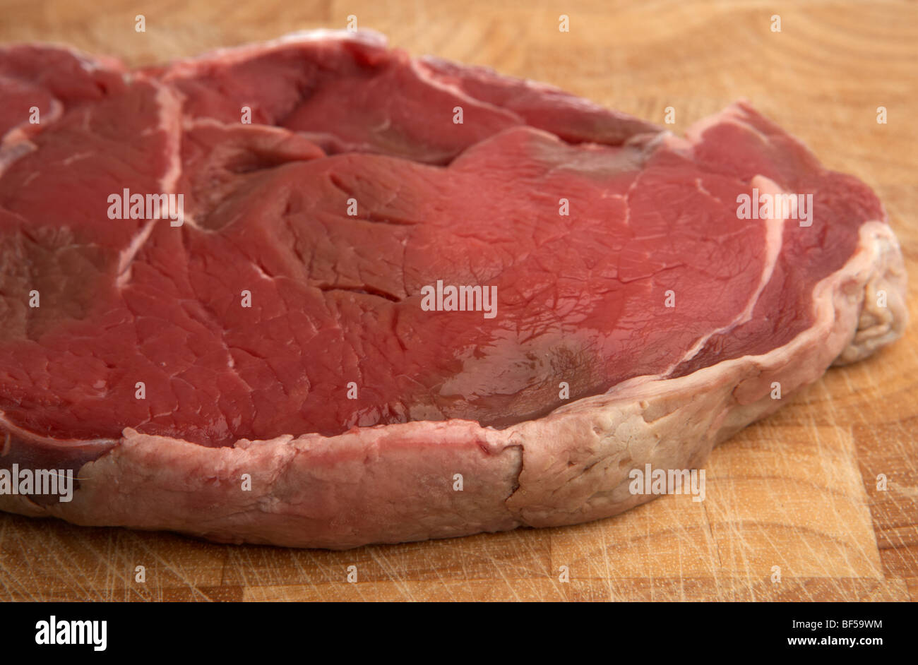 close up of the fat rind of a raw slice of chump steak from organic longhorn irish cows on a wooden butchers block Stock Photo