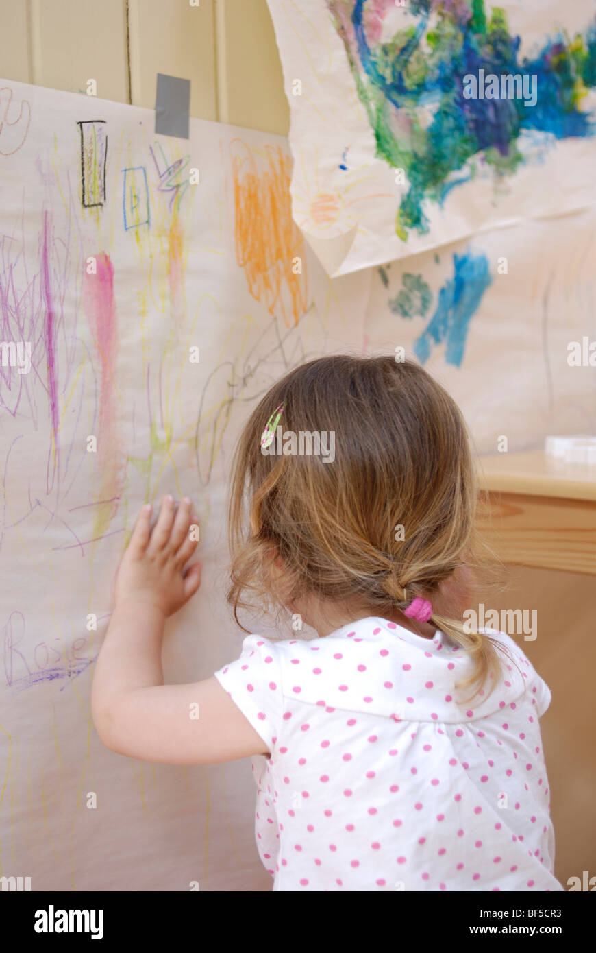 Young girl, three years old, drawing with crayons surrounded by her art. Stock Photo
