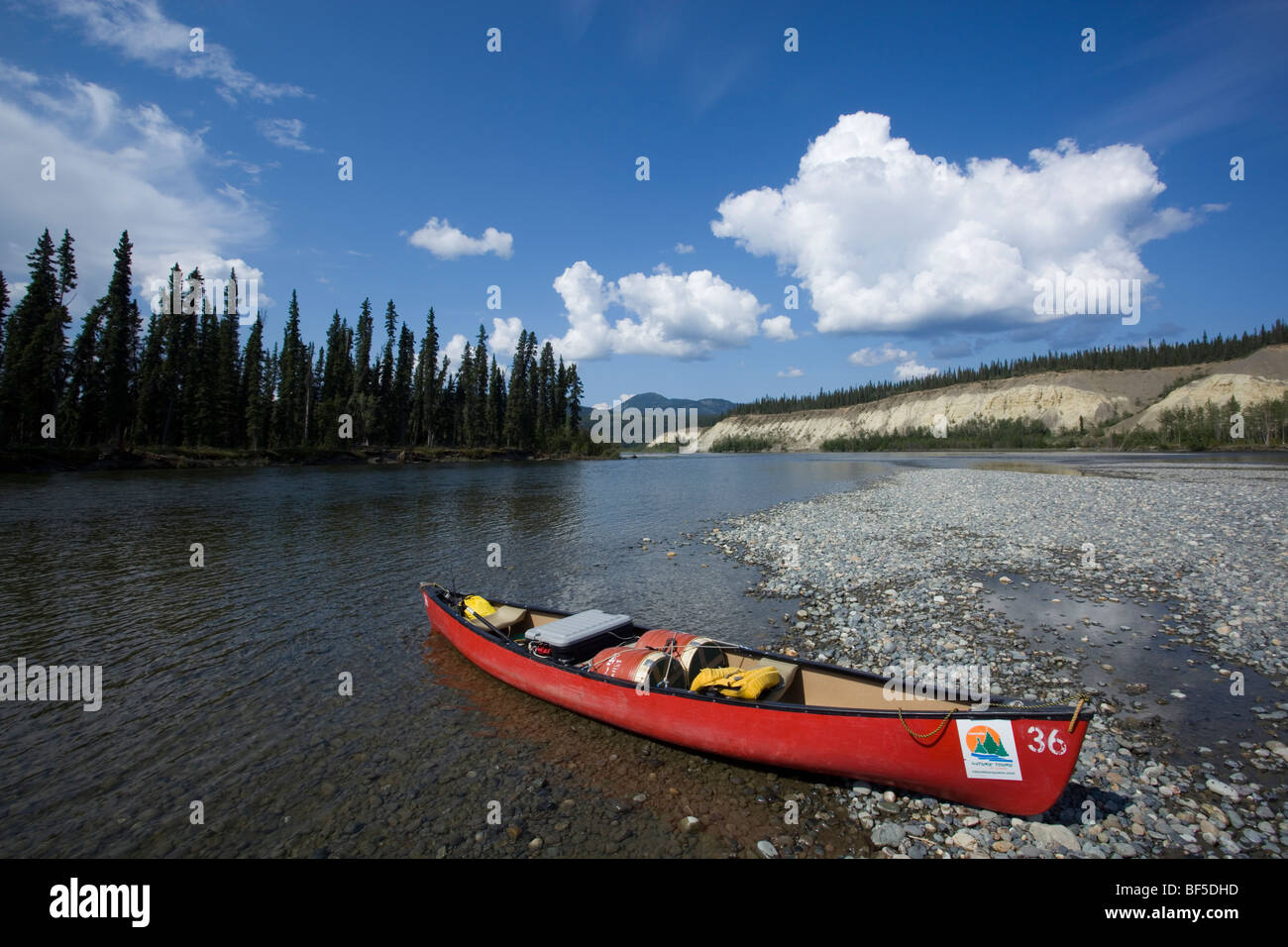 Loaded canoe on gravel bar, Teslin River, water formed landscape, high cut bank behind, Yukon Territory, Canada Stock Photo