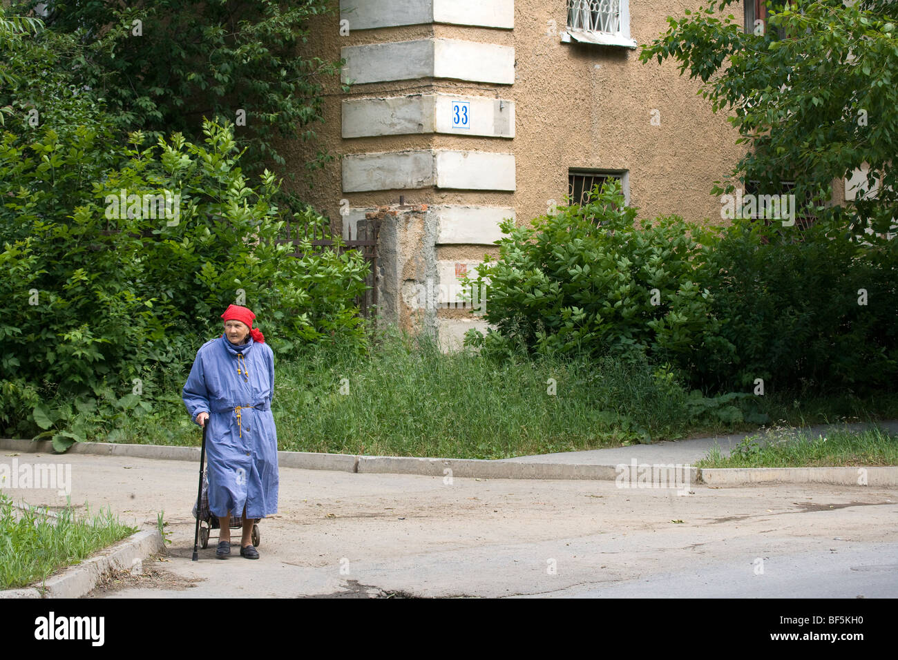 Elderly woman with shopping trolley on road outside social housing apartment, Ekaterinburg, Urals, Russia Stock Photo